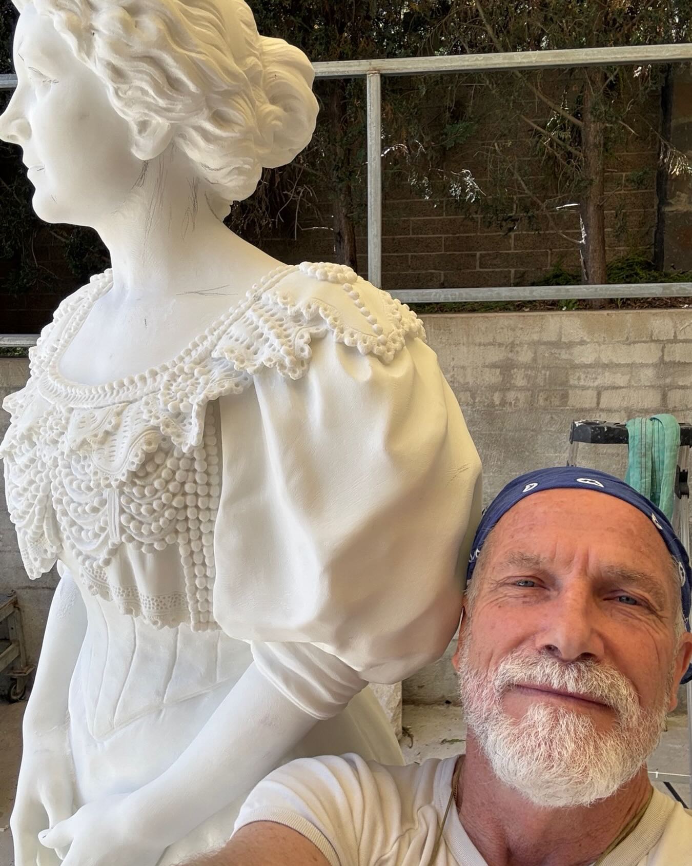Un hombre posa con una escultura de mármol de una mujer.