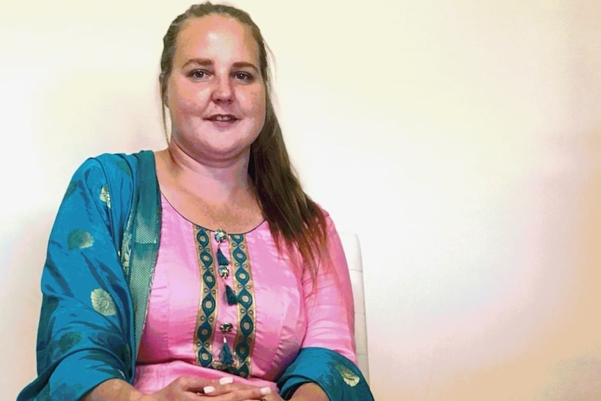 A woman sits with her hands folded on her lap looking into the camera and smiling