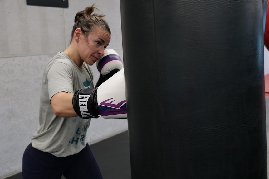 Woman hitting punching bag with right boxing glove