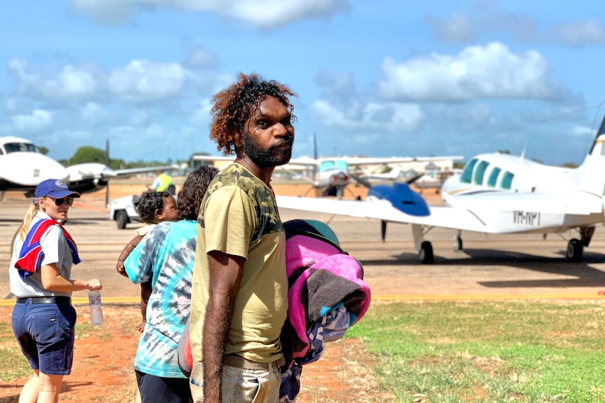 An Aboriginal man holding a beard stands in front of the small aeroplane he's about to board