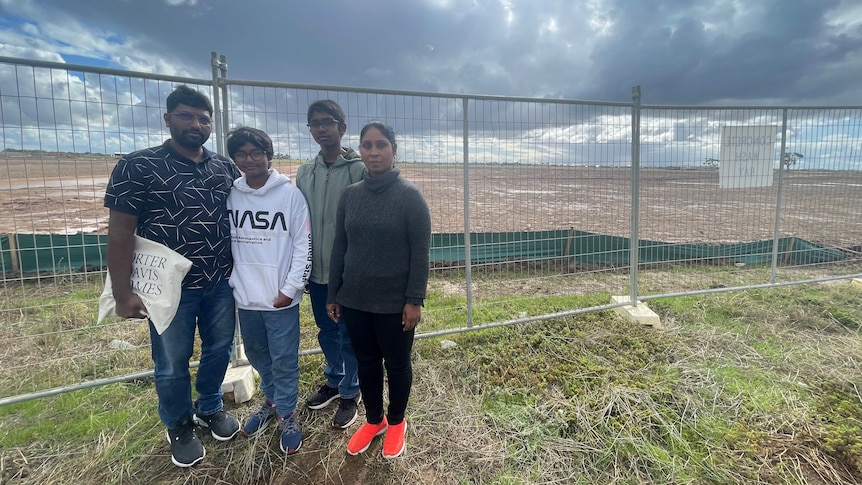 A family of four stand in front of a temporary fence with dark clouds looming above.