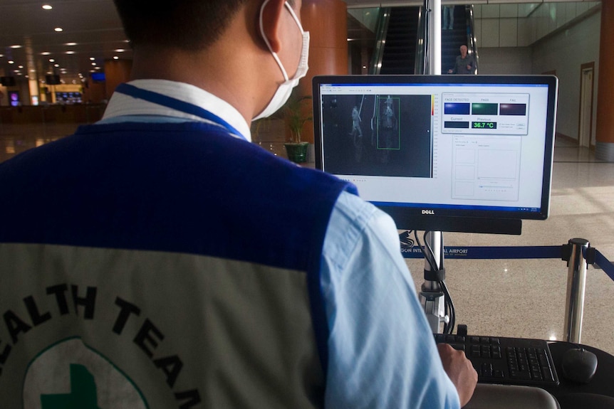 An airport staff member reads a computer screen to check the body temperatures of passengers.