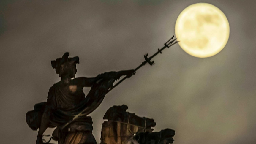 The moon in the sky sits at the pitchfork tip of the Maritime Prowess statue