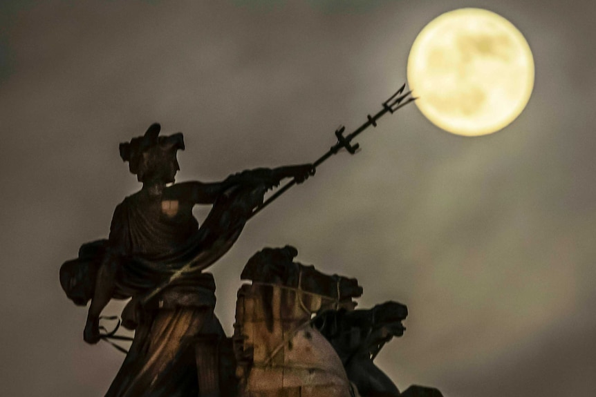 The moon in the sky sits at the pitchfork tip of the Maritime Prowess statue