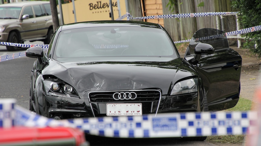 A dark-coloured, damaged Audi sedan in an area cordoned off with police tape.