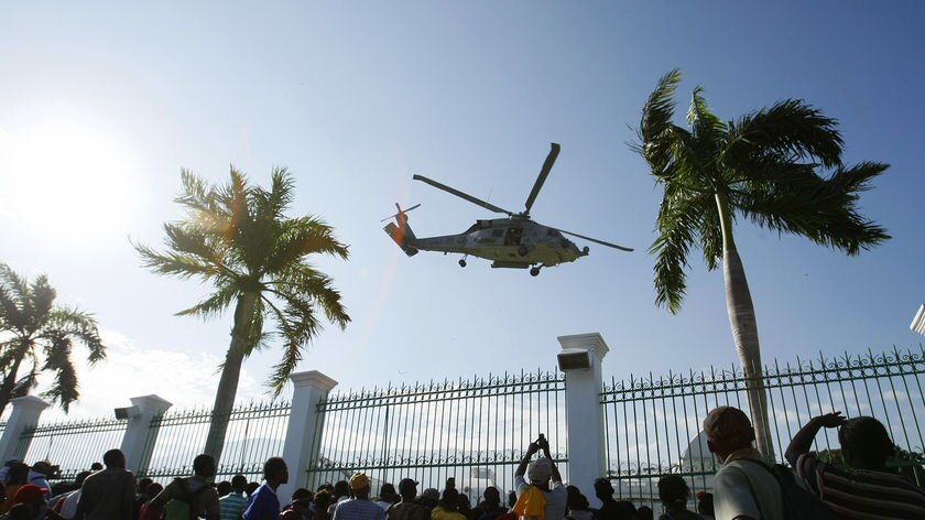 People gather around the presidential palace to watch a helicopter land with supplies and US troops