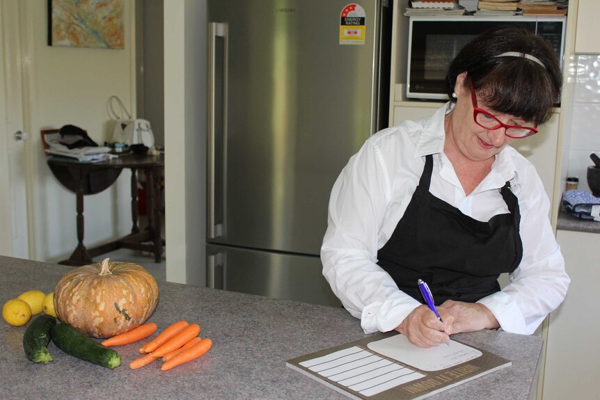 Linda Danvers in her kitchen writing a grocery list for a prospective client.