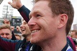 Eoin Morgan holds the Cricket World Cup trophy with his team behind him