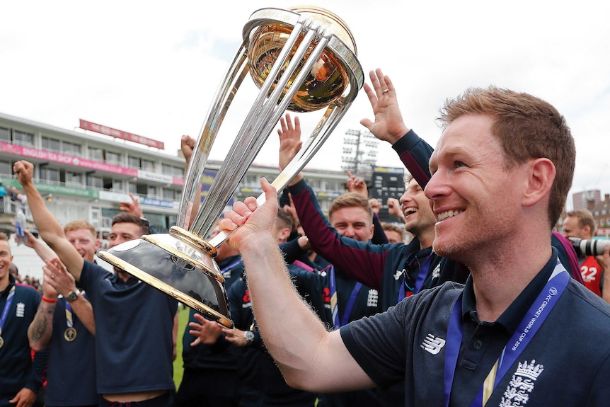 Eoin Morgan holds the Cricket World Cup trophy with his team behind him