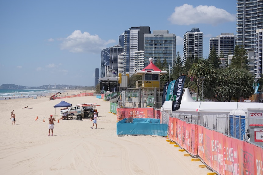 A beach on the left with highrises on the right, bright orange barricade separating the sand from the footpath