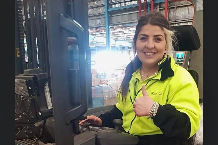 A woman drives a forklift and gives a thumbs up