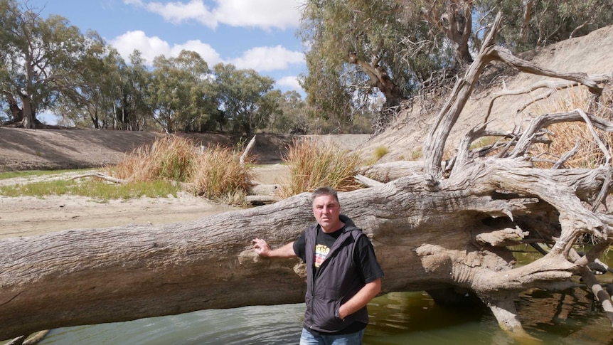 Graeme McCrabb leaning against a fallen tree in the Darling River at Menindee, submerged almost to his knees