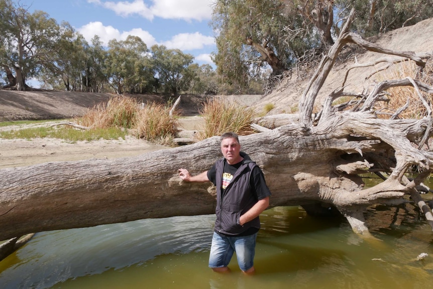 Graeme McCrabb leaning against a fallen tree in the Darling River at Menindee, submerged almost to his knees