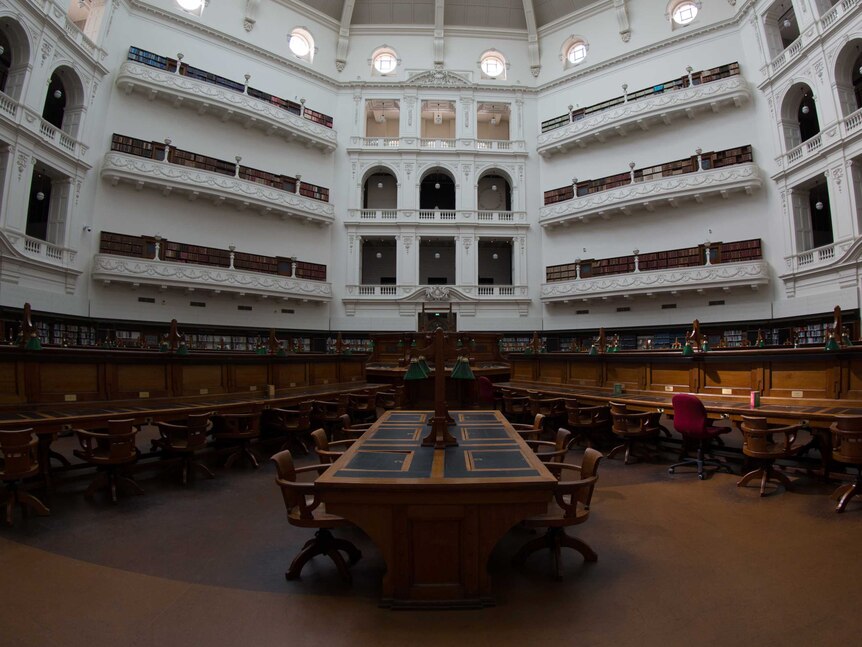 Empty desks on the ground floor of the State Library Victoria dome reading room, one chair lit by sunlight