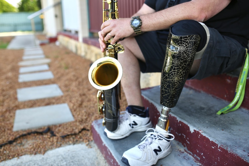 A close up of Andrew Fairbairn's prosthetic leg and saxaphone.