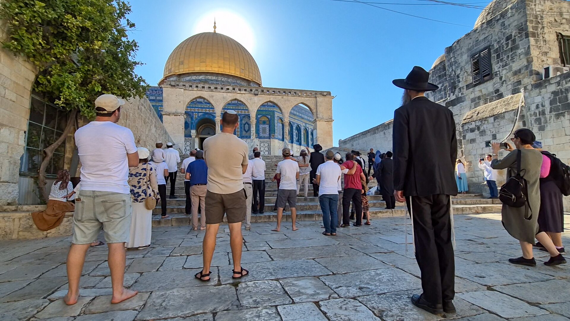 Jews stand in a paved area near steps leading to the golden roofed Dome of the Rock.
