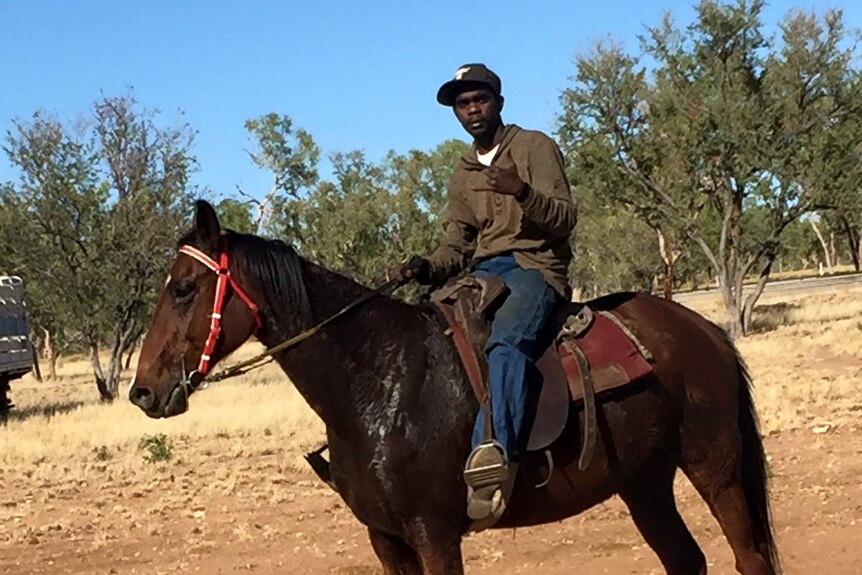 A man in jeans and an army green shirt on top of a horse