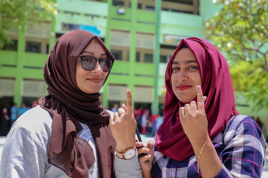 Two young Maldivian women raise their index fingers which is stained with ink.