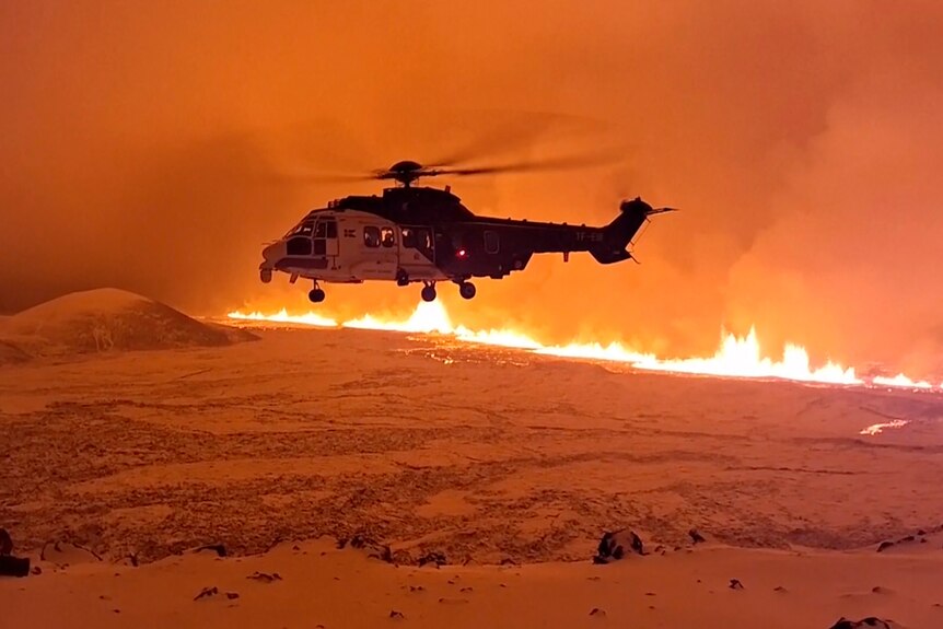 Helicopter in air above line of lava in the distance 