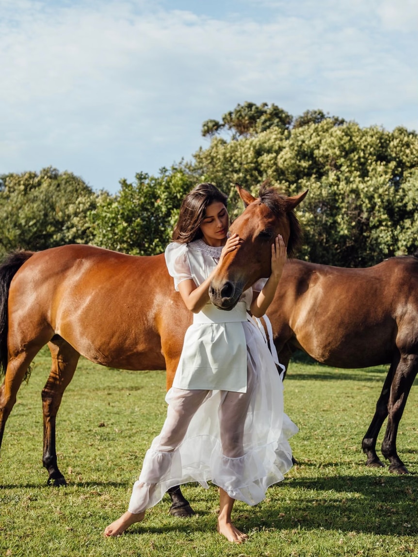 A model wearing Elizabeth Murray's clothes while posing with a horse.