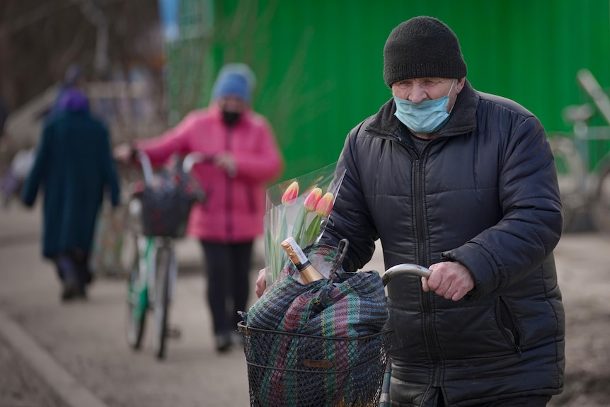 A man carries bags and a bunch of tulips on a bicycle.