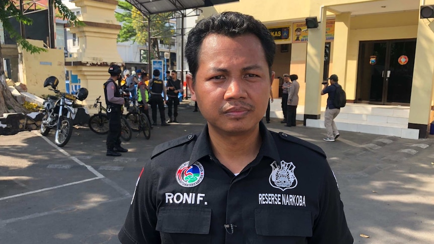 Police officer Roni Faisal looks solemn while police and others crowd in the background.