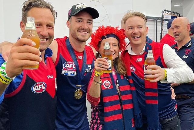 People in Melbourne Demons garb celebrating in the change rooms with a player.