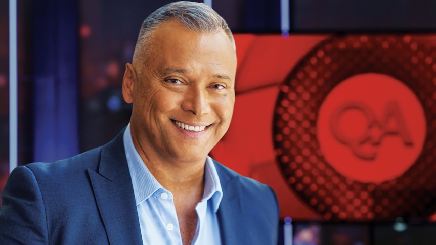 Q+A host Stan Grant in a blue suit in front of the Q+A logo.