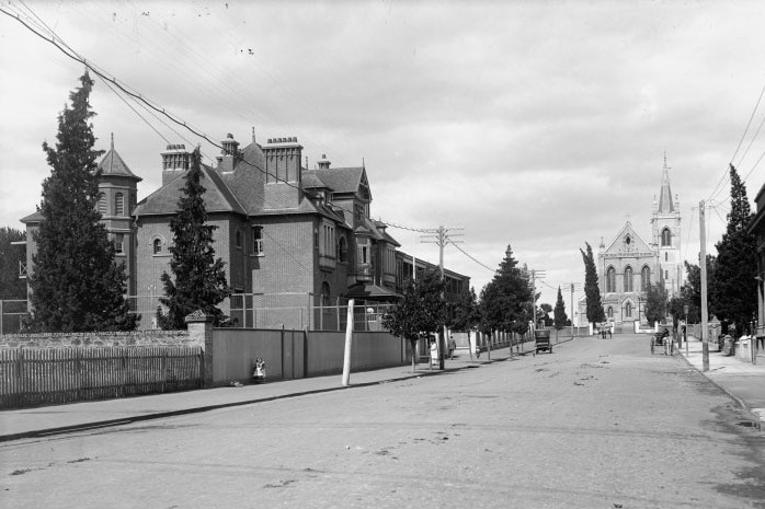 A 1906 street scape showing a large building to the left and a cathedral at the end of the street