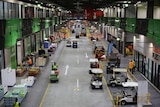 An elevated view of the inside of the Melbourne Market, with forklifts and workers moving down a concrete corridor.