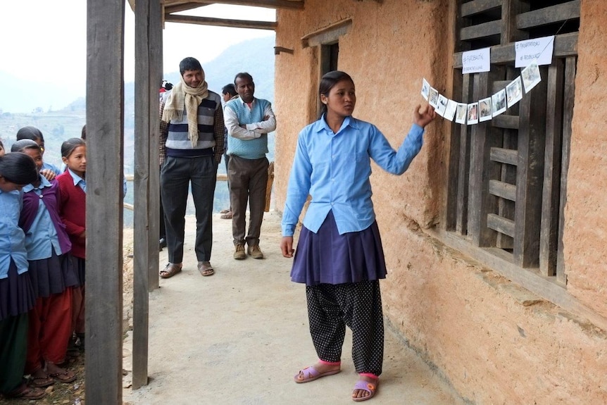 Nepali woman stands in front of a string of polaroid photos and many young girls look on