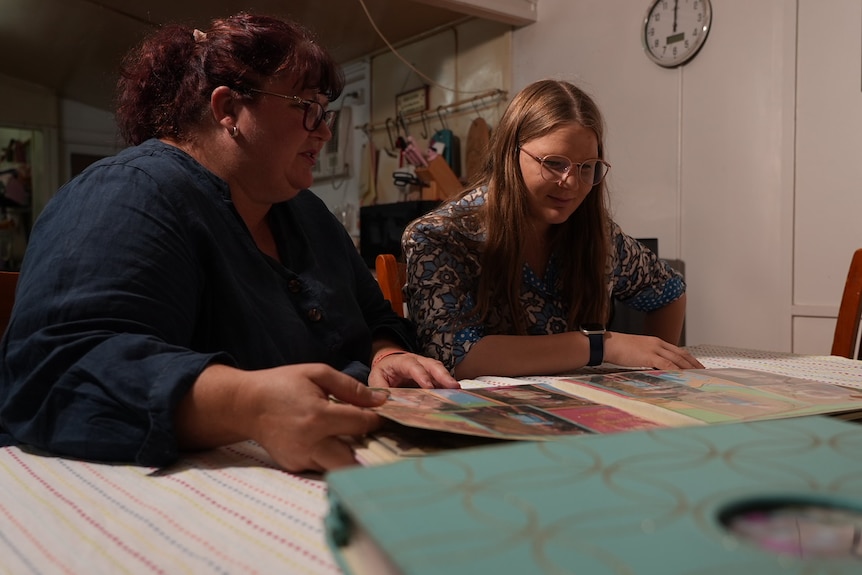 Woman and teenager sit at kitchen table looking at a family photo album