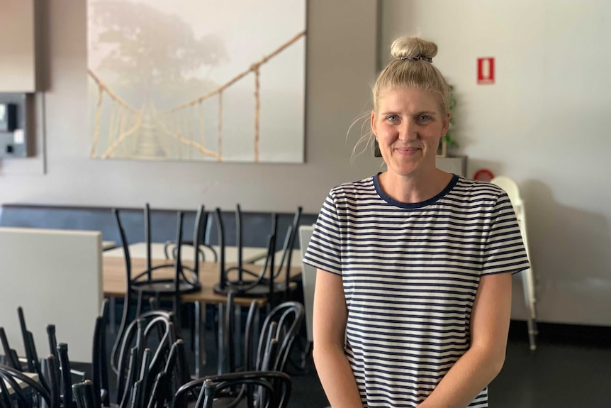 Karen Kiefer, wearing a striped top, stands in her cafe next to chairs on a table.