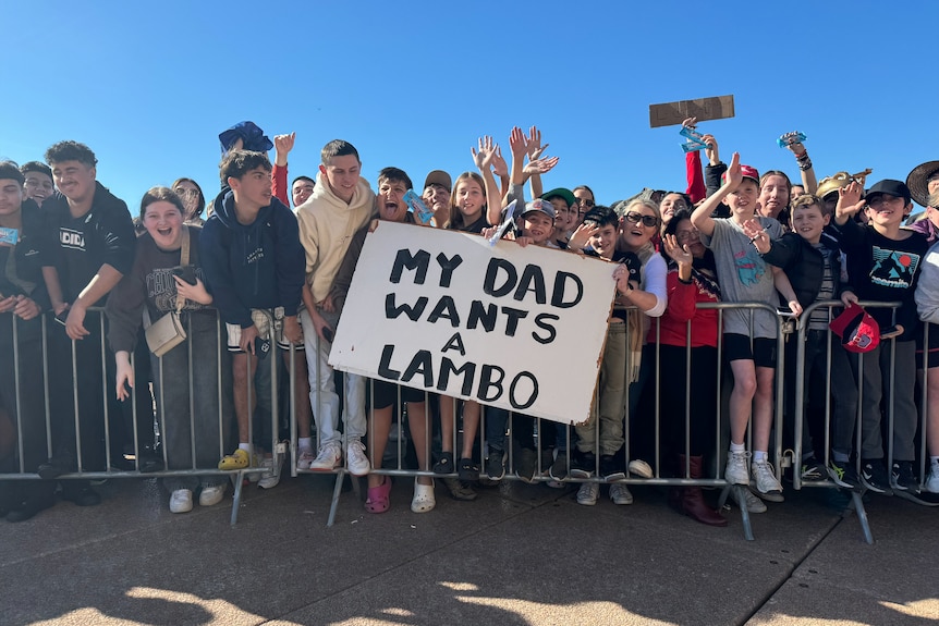 A group of children hold a sign saying my dad wants a lambo