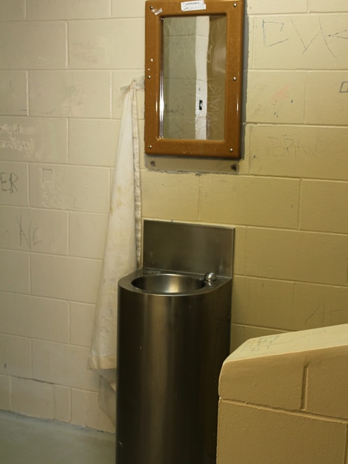 A squat metal sink and a small mirror. A white hand towel hangs from the mirror.