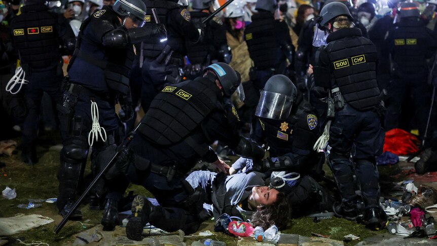 A protestor is held on the ground by police in helmets in a crowd