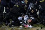 A protestor is held on the ground by police in helmets in a crowd