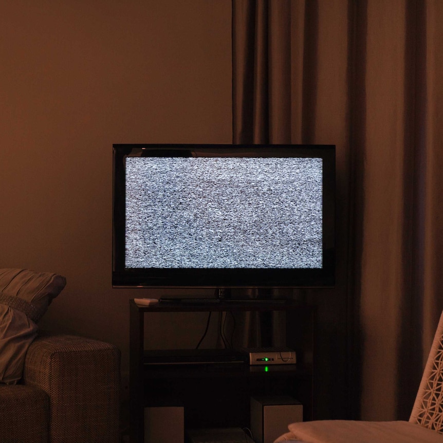 Static fuzz on TV, in corner of a dimly lit lounge room, with curtain in background.