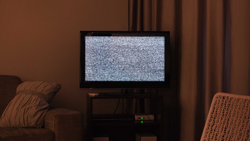 Static fuzz on TV, in corner of a dimly lit lounge room, with curtain in background.