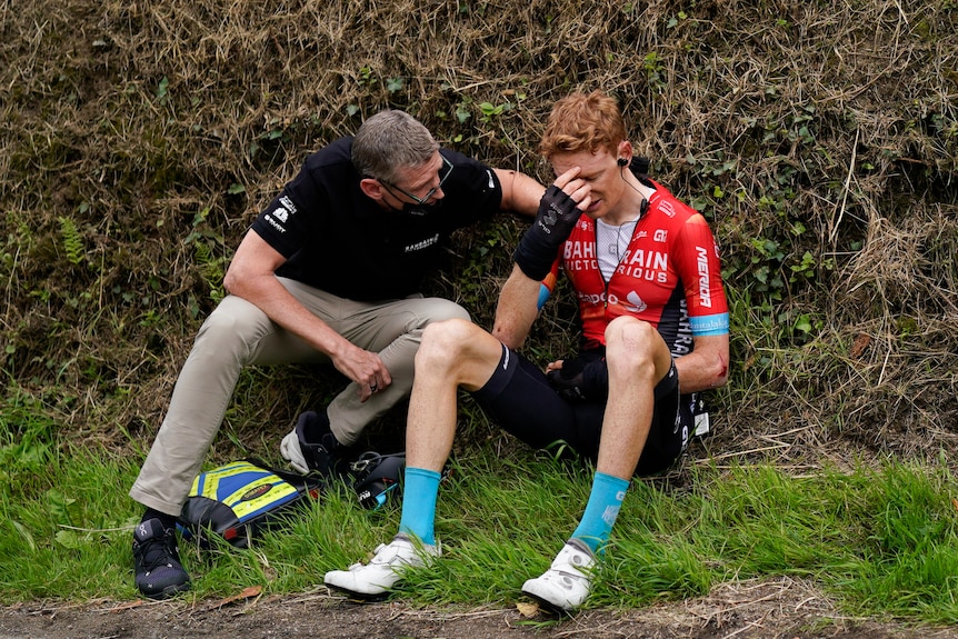 Jack Haig sits in tears being comforted by a team staff member.