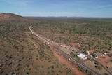 an aerials shot shows a long line of cars along a road leading to a border check point