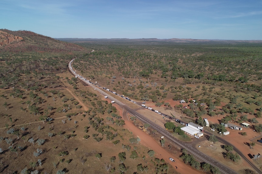 an aerials shot shows a long line of cars along a road leading to a border check point