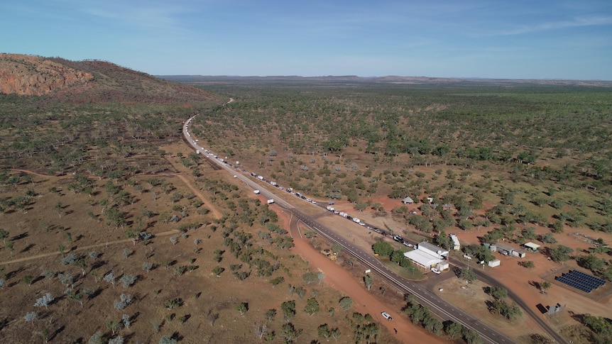 an aerials shot shows a long line of cars along a road leading to a border check point