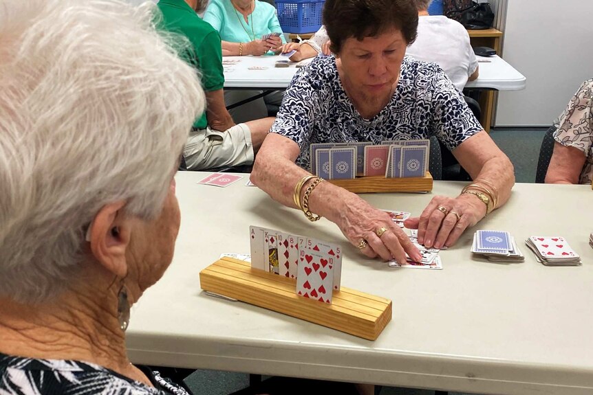 Older citizens play cards together in a classroom.
