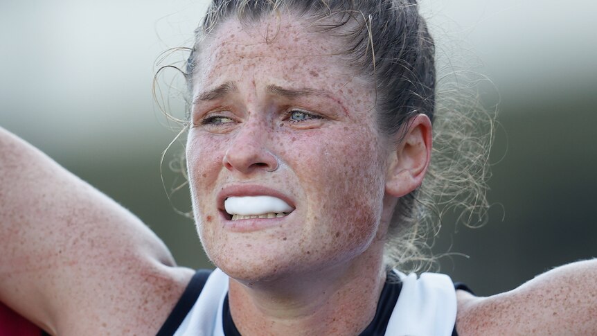 A close up of Bri Davey looking devastated as she is helped from the field after a knee injury