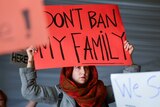 A woman holds a red sign reading don't ban my family