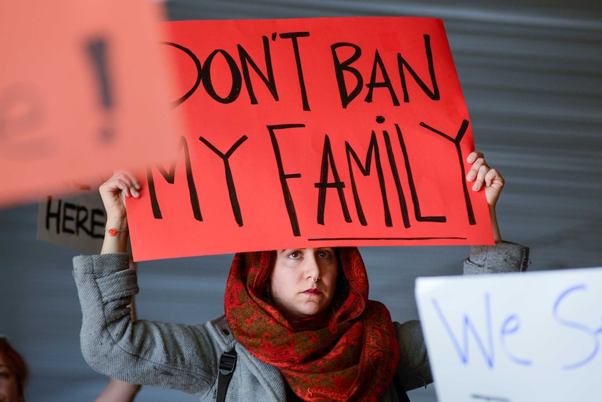 A woman holds a red sign reading don't ban my family