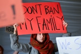 A woman holds a red sign reading don't ban my family