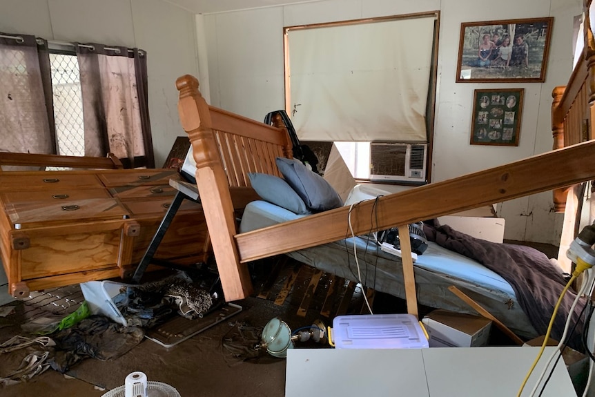 Displaced bed frame, mattress, furniture inside house, covered in mud.