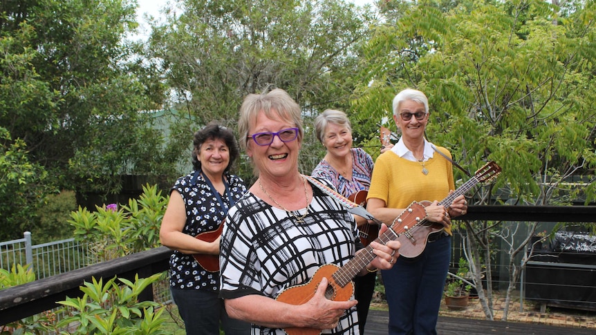 Four women with ukulele's stand outside